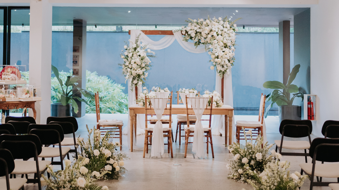 Elegant indoor wedding ceremony setup decorated with white flowers and wooden chairs.