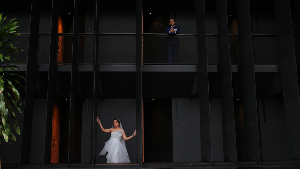 Bride and groom posing on separate levels of a dramatic dark modern building.