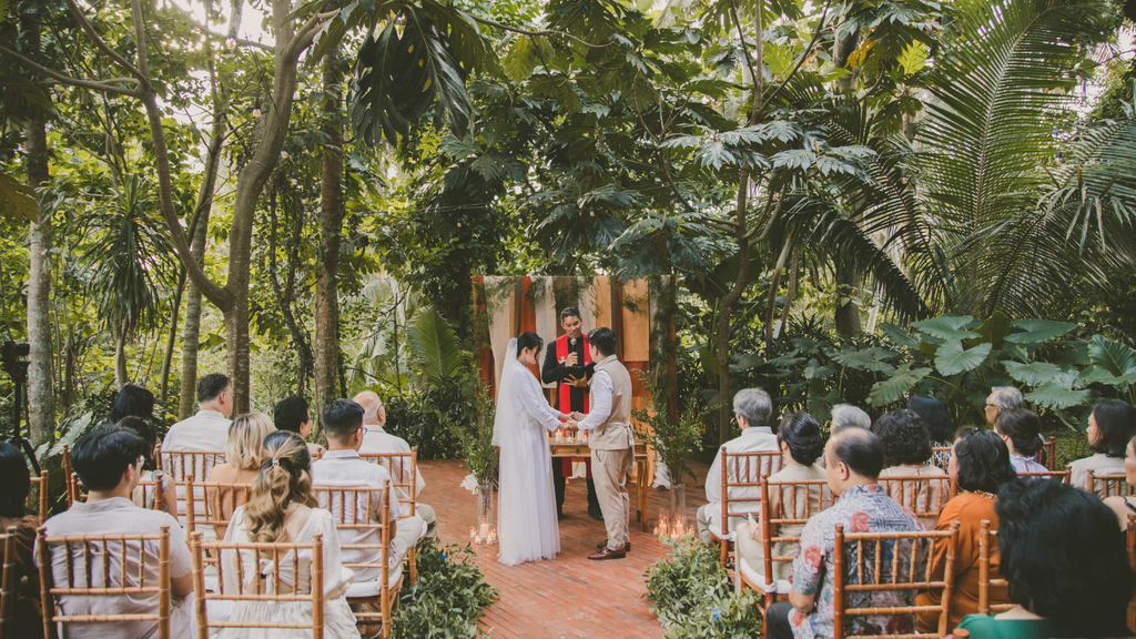 Couple exchanging vows during an intimate outdoor wedding ceremony surrounded by lush tropical greenery.