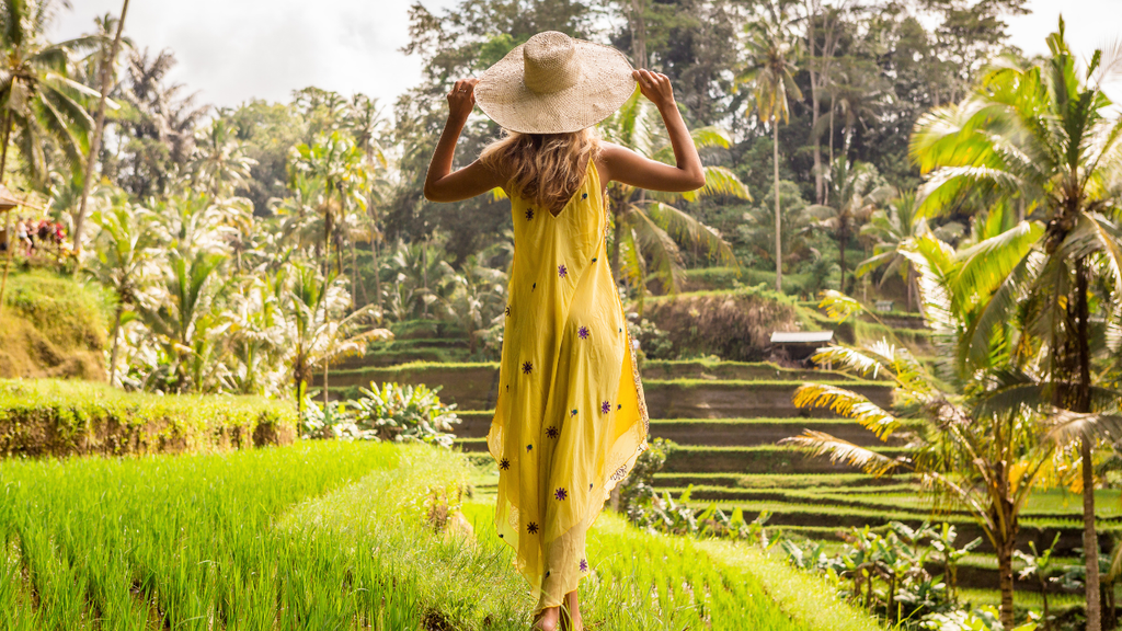 Woman in a yellow dress walking through lush green rice terraces in Bali.