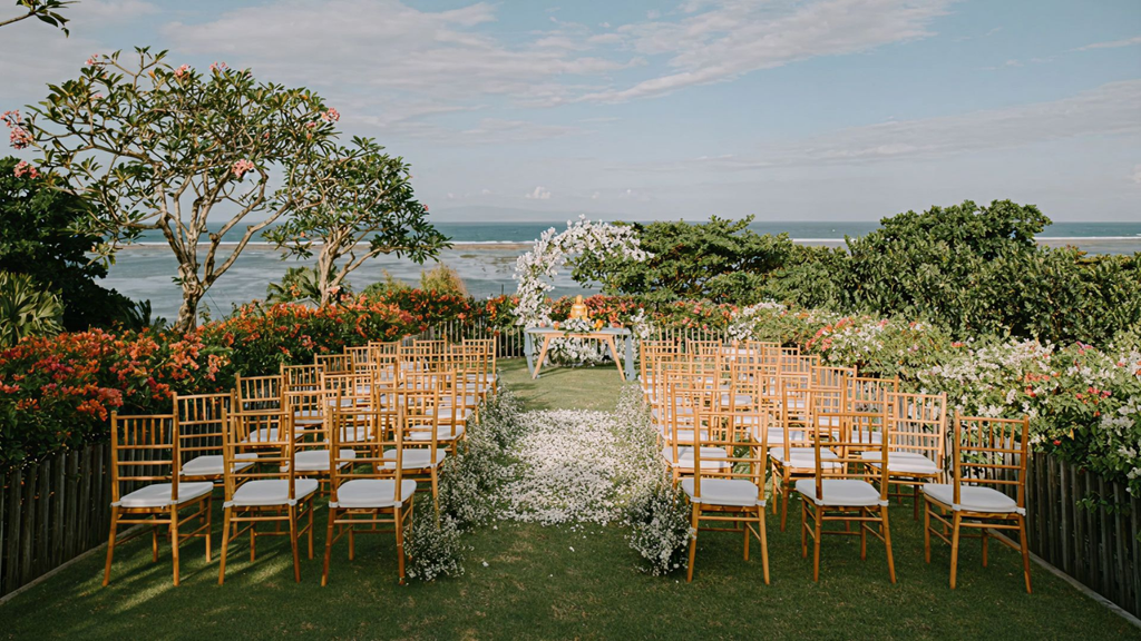 Intimate oceanfront wedding ceremony setup with gold chairs, white floral arrangements, and a garden overlooking the sea.