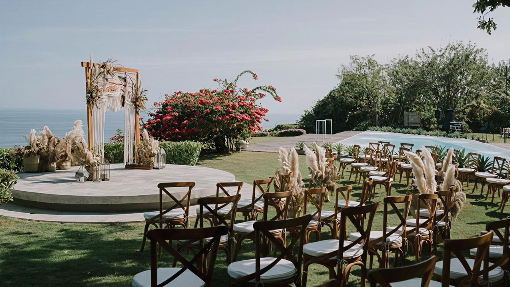 Romantic cliffside wedding ceremony setup with a rustic wooden arch, pampas grass decorations, and ocean views.